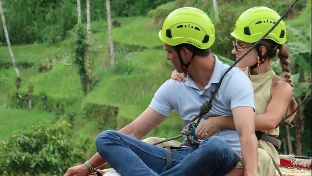 Couple Wearing Bright Green Helmets Sitting on a Zip-line Rope, Harnessed Outdoors in a Green Forest Area. - Regio Politica