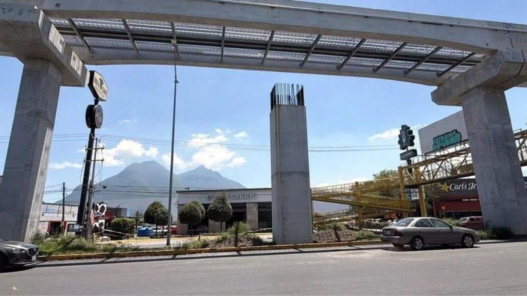 Urban Street Scene with Elevated Concrete Tracks Under Construction, Cars Driving By, and Distant Mountains in the Background. - Regio Politica