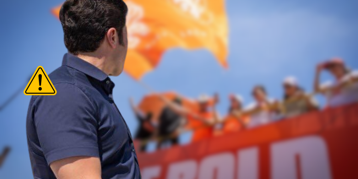 Bloque 2- Junio - Regio Politica Man Seen from Behind at a Rally, Facing a Cheering Crowd with an Orange Banner and a Warning Icon Overlaid on the Left Side. - Regio Politica