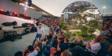 Male Performer on a Stage Waving to a Large Seated Audience at an Outdoor Concert, Sunset Sky Above the Venue. - Regio Politica