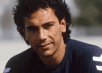 Close-up of a Man with Dark Curly Hair Wearing a Navy Shirt, Outdoors Near a Beach. - Regio Politica
